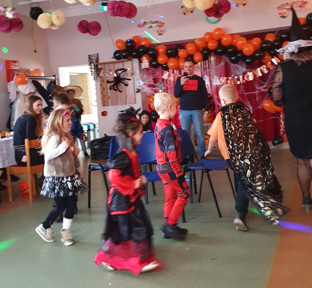 Dzieci w kostiumach tańczą w sali wystrojonej dekoracjami na Halloween