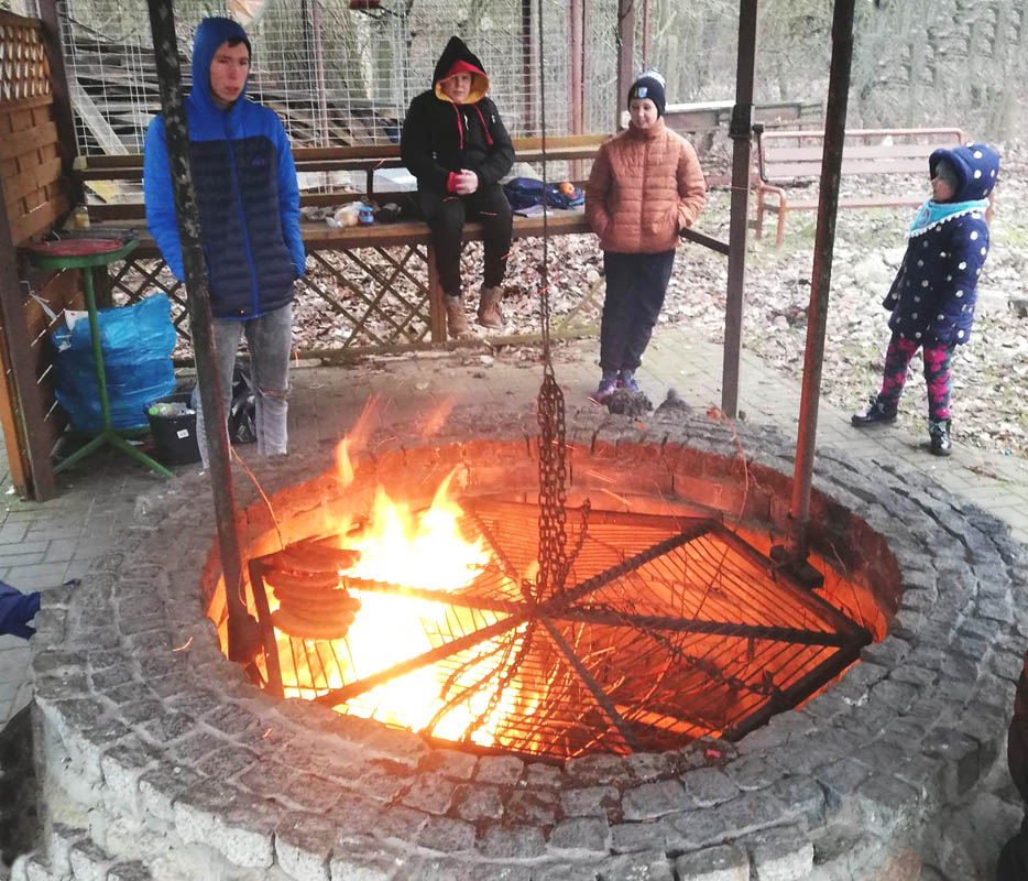 W centrum zdjęcia ognisko z rusztem nad nim, wokół niego czwórka dzieci