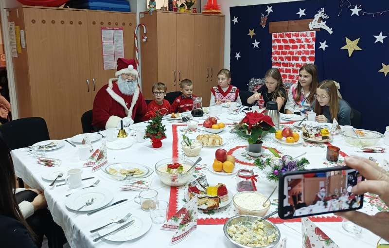 Przy zastawionym stole siedzą dzieci oraz św. Mikołaj